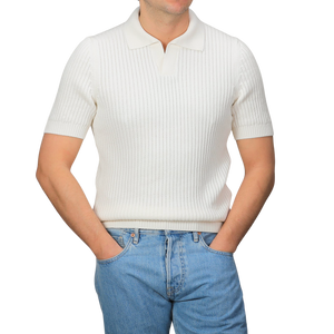 A person dons the Off-White Organic Cotton Polo Shirt by Gran Sasso, featuring a chunky-knit and short sleeves, paired with slim-fit blue jeans, hands in pockets against a grey background.