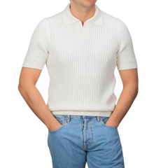 A person dons the Off-White Organic Cotton Polo Shirt by Gran Sasso, featuring a chunky-knit and short sleeves, paired with slim-fit blue jeans, hands in pockets against a grey background.