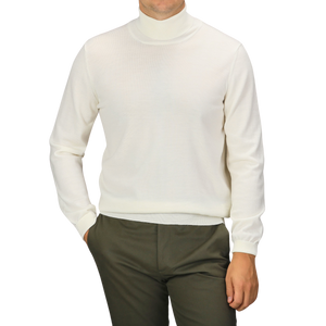 A person wearing an Off White Extra Fine Merino Roll Neck sweater from Gran Sasso and green pants, with their right hand in their pocket.