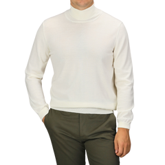 A person wearing an Off White Extra Fine Merino Roll Neck sweater from Gran Sasso and green pants, with their right hand in their pocket.