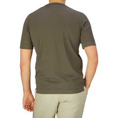 A person photographed from behind wearing a Gran Sasso olive green organic cotton t-shirt and cream-colored pants against a neutral background.