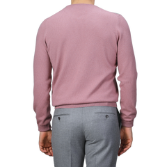 A person wearing a Gran Sasso Pale Pink Cashmere Crewneck Sweater and gray pants, photographed from the back against a gray background, embodies the elegance of sustainable knitwear.