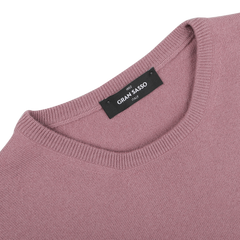 A close-up of a folded Pale Pink Cashmere Crewneck Sweater highlights its luxurious texture. The black label features "Gran Sasso" in white text, emphasizing the brand's commitment to sustainable knitwear.