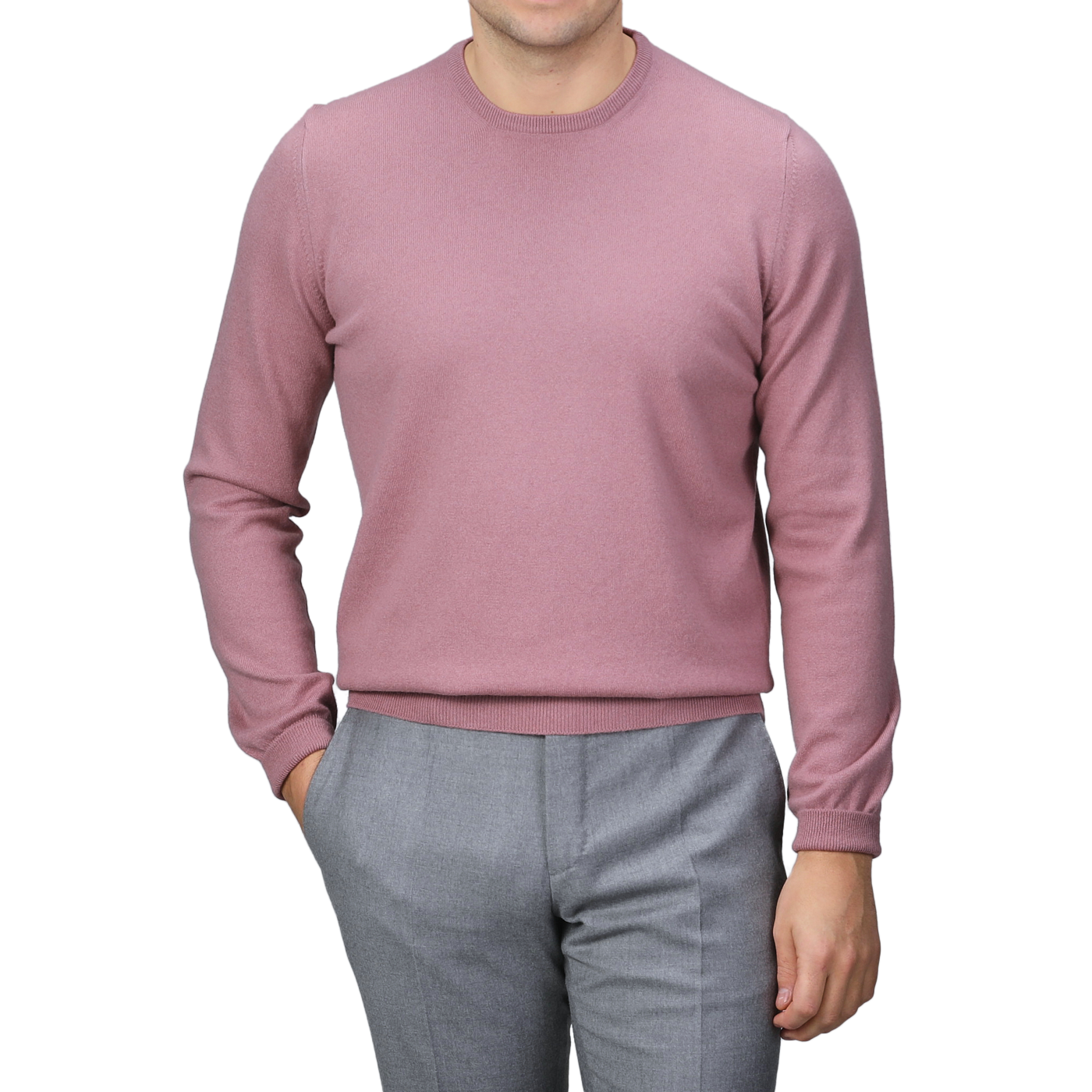 A person wearing a Pale Pink Cashmere Crewneck Sweater by Gran Sasso and gray pants stands with one hand in their pocket against a gray background.