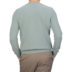 An individual is facing away from the camera against a gray background, wearing a Sage Green Egyptian Cotton Crewneck Sweater by Gran Sasso paired with beige pants.