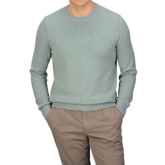 A person wears a Sage Green Egyptian Cotton Crewneck Sweater by Gran Sasso with beige pants, hands in pockets against a plain gray background.