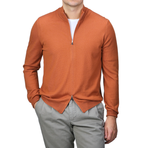 A person is stylishly wearing a Sienna Brown Extrafine Merino Wool Zip Cardigan from Gran Sasso, featuring its elegant merino wool fabric over a white shirt with gray pants.