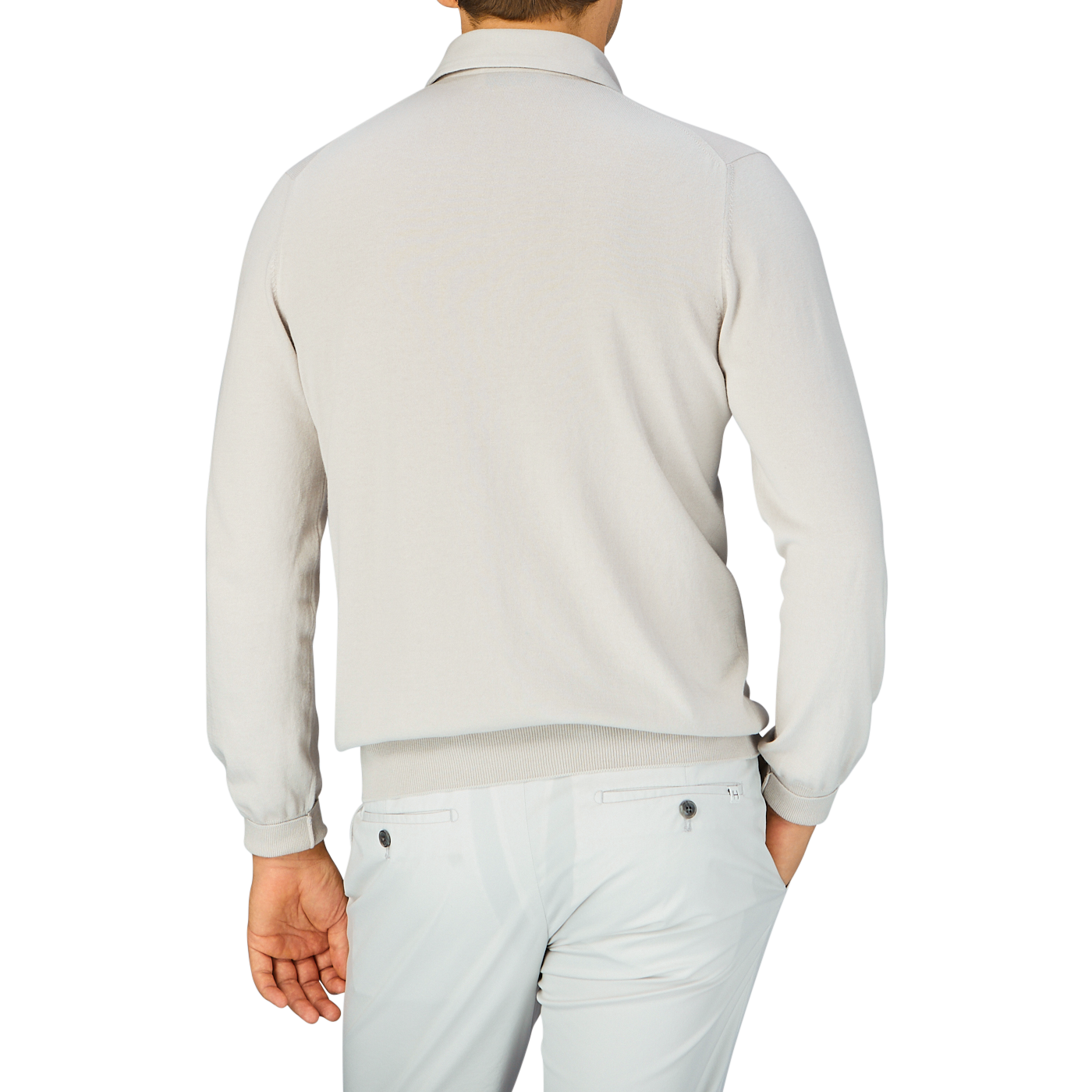A man viewed from behind wearing a taupe beige Gran Sasso long-sleeved polo shirt made of organic cotton and white pants.