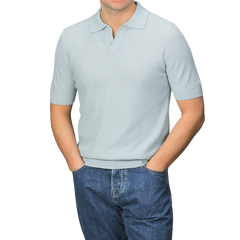 A person wearing a slim fit, turquoise cotton linen polo shirt by Gran Sasso and blue jeans stands with hands in pockets against a plain grey background.