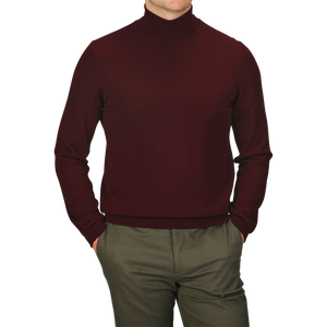 A person wearing a slim fit, Wine Melange Extra Fine Merino Roll Neck sweater by Gran Sasso and green pants, with hands in pockets against a white background. The person's face is not visible.