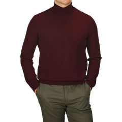 A person wearing a slim fit, Wine Melange Extra Fine Merino Roll Neck sweater by Gran Sasso and green pants, with hands in pockets against a white background. The person's face is not visible.