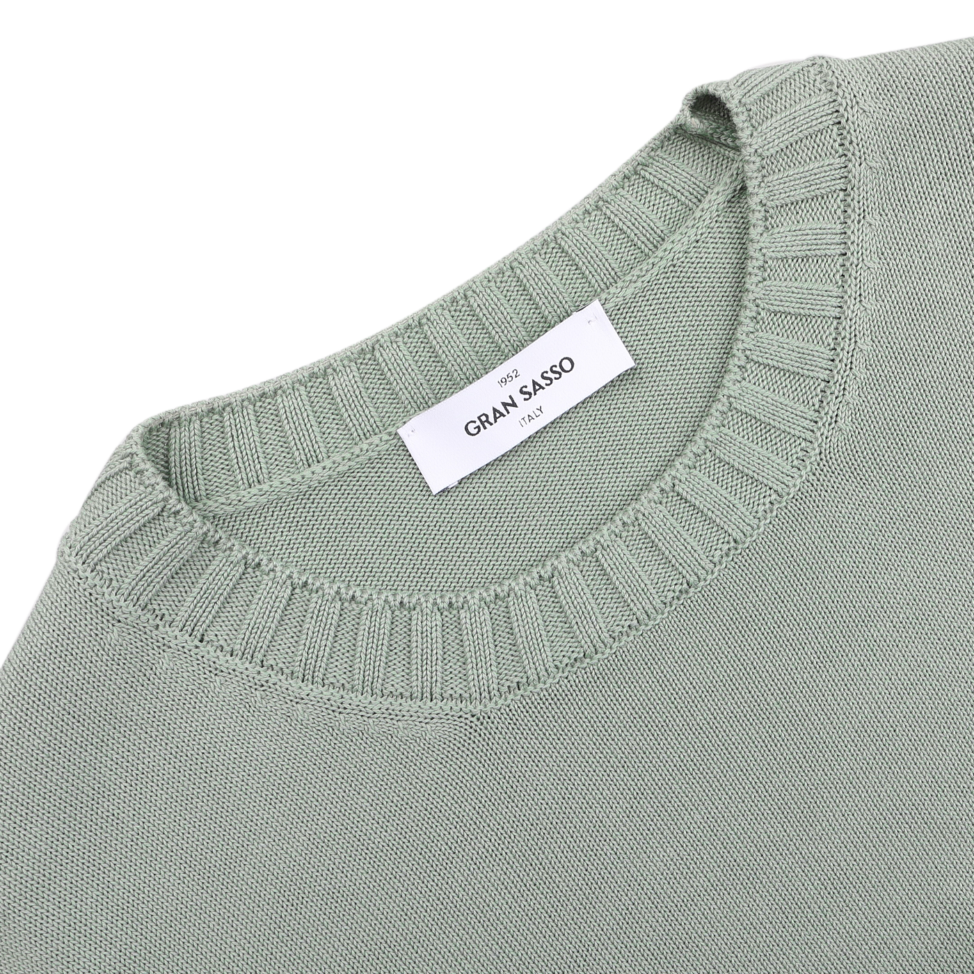 Close-up of a folded sage green crewneck sweater by Gran Sasso with a ribbed neckline, made from luxurious Egyptian cotton. A white label states "Gran Sasso" and "Made in Italy.