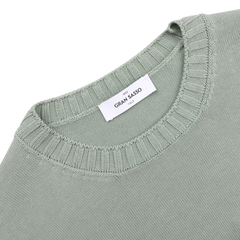 Close-up of a folded sage green crewneck sweater by Gran Sasso with a ribbed neckline, made from luxurious Egyptian cotton. A white label states "Gran Sasso" and "Made in Italy.