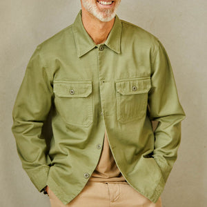 A man wearing a grass green Tela Genova Cotton Overshirt with button closure and tan pants.