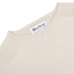 Close-up of the Almond White Extrafine Lambswool Crewneck sweater from Harley of Scotland, featuring a "Harley" label that indicates it's made in Scotland and size 'M'.