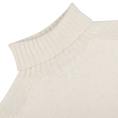 This close-up showcases the Almond White Extrafine Lambswool Rollneck from Harley of Scotland, featuring a ribbed turtleneck and raglan sleeve.