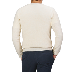 A person wearing an Almond White Extrafine Lambswool Crewneck by Harley of Scotland and dark pants, viewed from the back with hands in pockets.