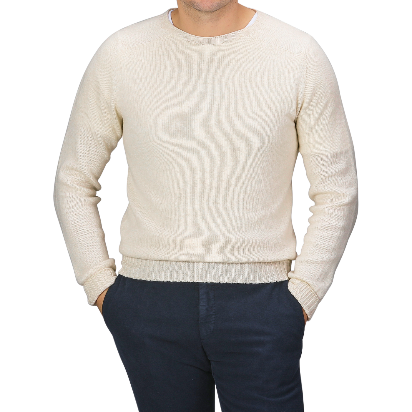 A person wearing the Almond White Extrafine Lambswool Crewneck by Harley of Scotland and dark pants stands with hands in their pockets against a gray background.