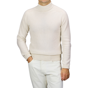 A person wearing a Harley of Scotland Almond White Extrafine Lambswool Rollneck and white pants stands against a neutral background.