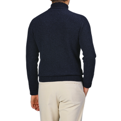 A person wearing a Harley of Scotland Cosmos Blue Extrafine Lambswool Rollneck sweater and light pants stands facing away against a neutral background.