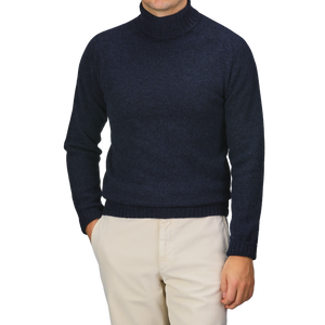 A person wearing the Cosmos Blue Extrafine Lambswool Rollneck by Harley of Scotland paired with beige pants, with their arms relaxed at their sides.