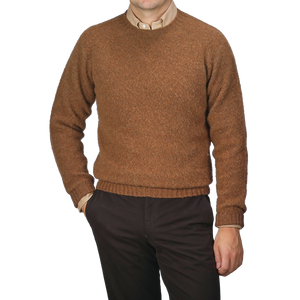 A person wearing a Pecan Brown Brushed Shaggy Wool Crewneck from Harley of Scotland and dark pants is standing with one hand in the pocket against a neutral background.