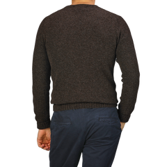 A person wearing a Porcupine Brown Extrafine Lambswool Crewneck by Harley of Scotland and navy pants stands facing away, with one hand in their pocket.