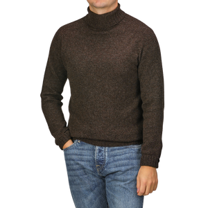 The person is wearing a Porcupine Brown Extrafine Lambswool Rollneck by Harley of Scotland paired with blue jeans, with one hand casually tucked in their pocket.