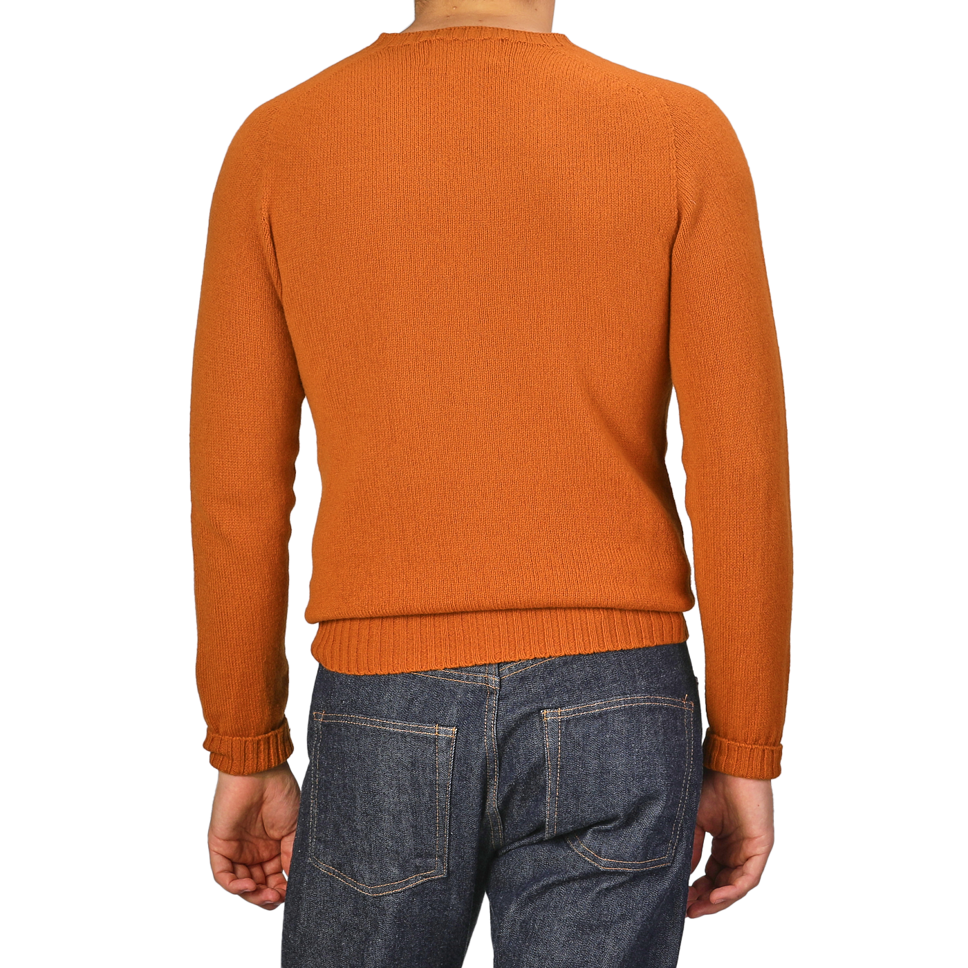 The scene captures someone wearing a Sienna Orange Extrafine Lambswool Crewneck from Harley of Scotland, paired with blue jeans.