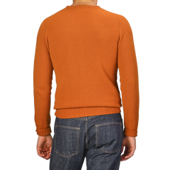 The scene captures someone wearing a Sienna Orange Extrafine Lambswool Crewneck from Harley of Scotland, paired with blue jeans.