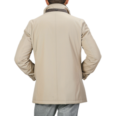 Rear view of a person wearing a luxurious Beige Loro Piana Wool Twill Jacket by Herno with a high collar and gray trousers, hands on hips.