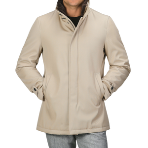 A person wearing a luxurious Beige Loro Piana Wool Twill Jacket by Herno with hands in pockets, over a black shirt and grey pants. The pure wool twill jacket features a high collar, button details on the cuffs, and offers both rain and wind resistance.