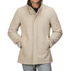 A person wearing a luxurious Beige Loro Piana Wool Twill Jacket by Herno with hands in pockets, over a black shirt and grey pants. The pure wool twill jacket features a high collar, button details on the cuffs, and offers both rain and wind resistance.