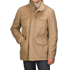 A person is wearing a Camel Beige Loro Piana Wool Field Jacket by Herno, featuring a high collar and flap pockets, with hands tucked in. The stylish jacket, equipped with Rain System technology, pairs perfectly with a turtleneck and jeans.