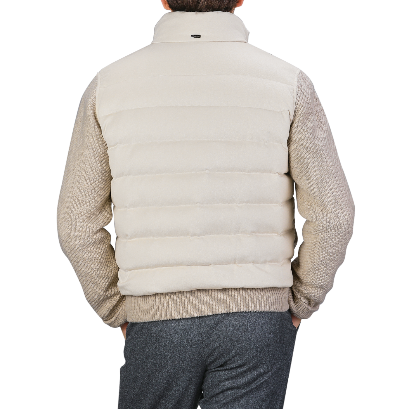 An individual wearing a cream beige cashmere silk bomber jacket by Herno over a knitted sweater and gray pants, seen from behind.