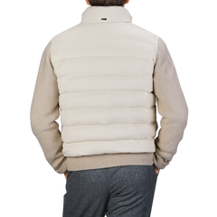 An individual wearing a cream beige cashmere silk bomber jacket by Herno over a knitted sweater and gray pants, seen from behind.