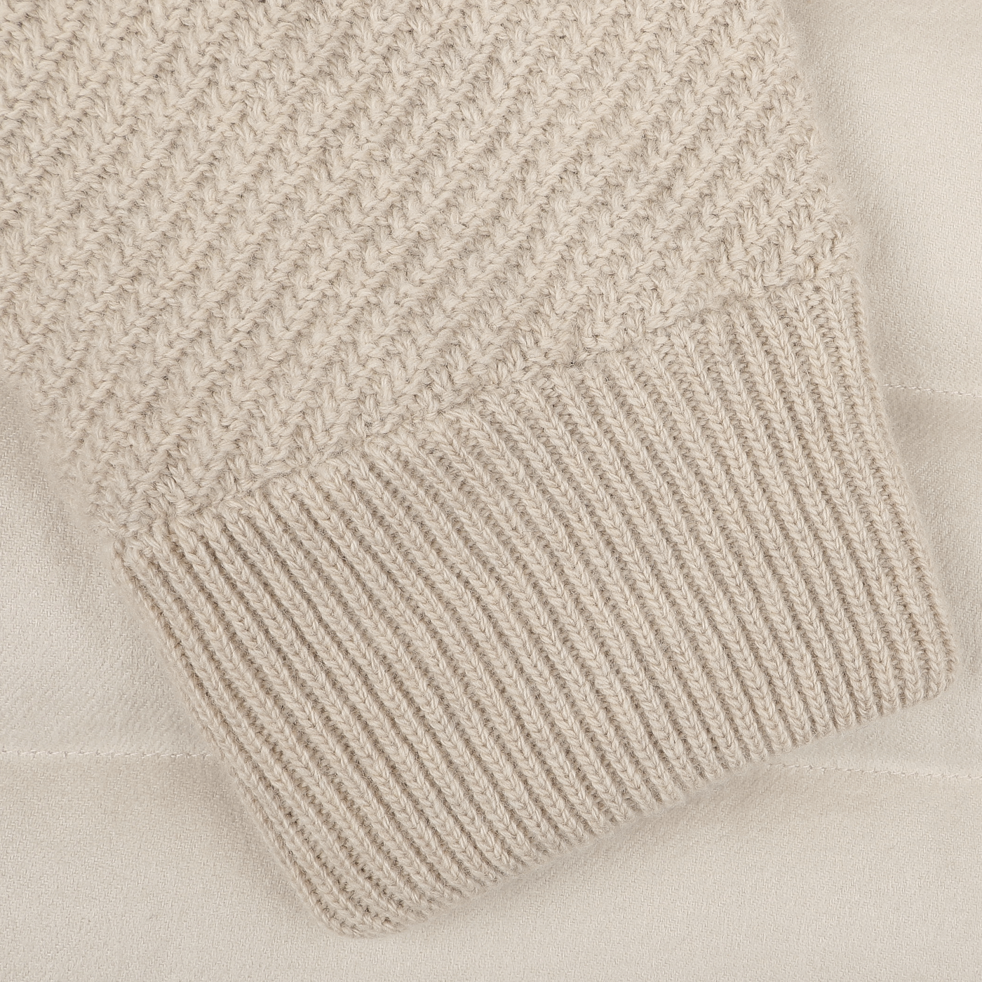 Close-up of a sleeve from the Herno Cream Beige Cashmere Silk Bomber Jacket, featuring a ribbed cuff and crafted from luxurious silk and cashmere, lying on a matching fabric background.