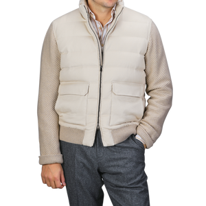 A person wearing a Herno Cream Beige Cashmere Silk Bomber Jacket over a striped shirt and gray pants stands with one hand in their pocket.