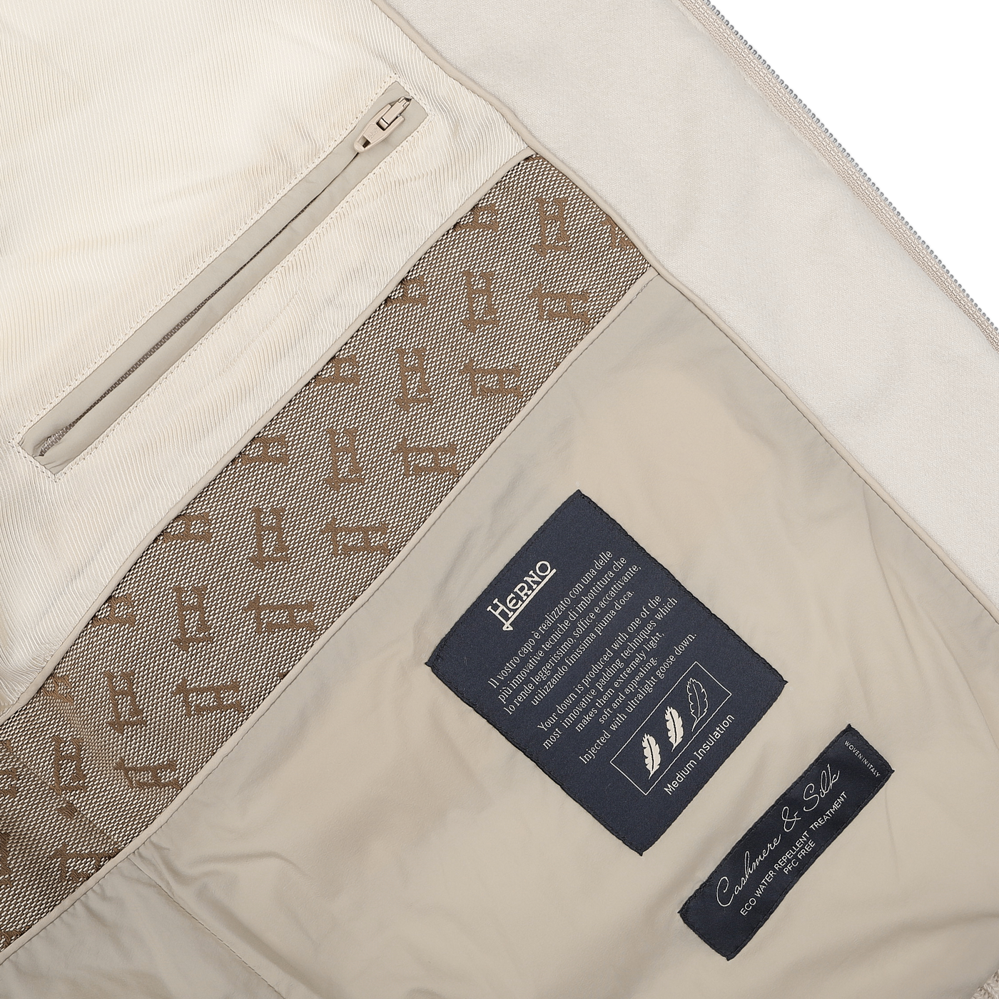 The interior of the Cream Beige Cashmere Silk Bomber Jacket by Herno features a zipper pocket, logo lining, and dark labels that read "Herno," "Goose Down," and provide care instructions for the silk and cashmere blend.