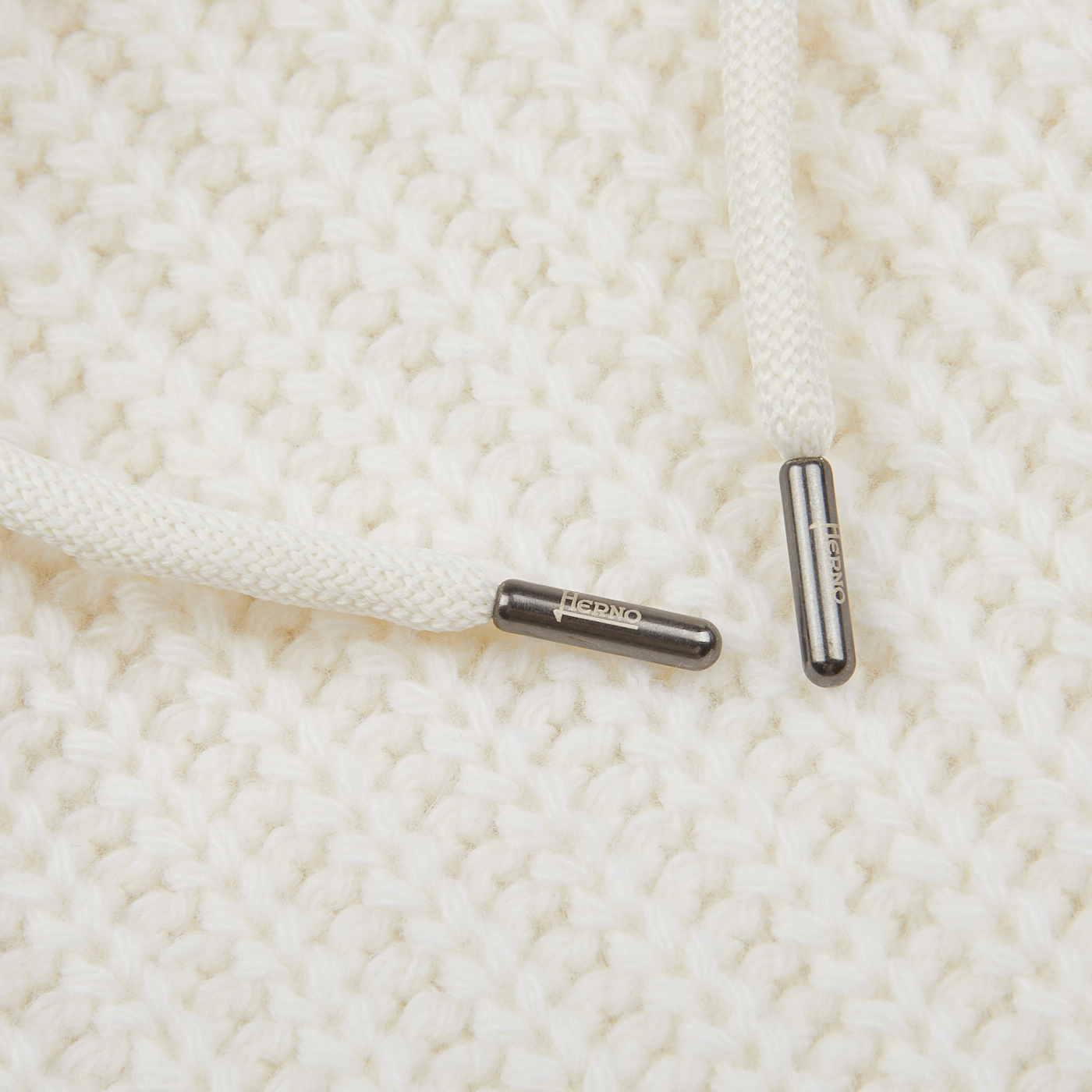 Close-up image of two white drawstrings with metallic tips labeled "HEDNO" on a textured virgin wool knitted fabric background from the Cream Wool Nylon Reversible Knitted Jacket by Herno.