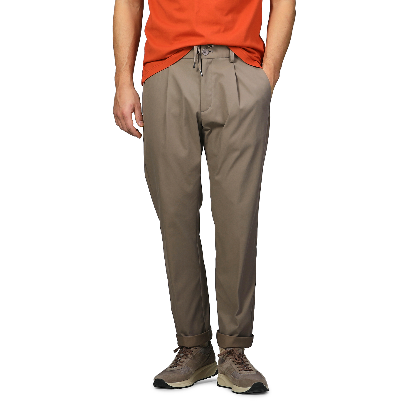 Dressed in an orange shirt, a person stands with hands in pockets, wearing sneakers and dark beige nylon stretch drawstring trousers by Herno.