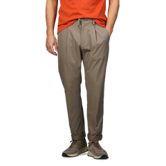 Dressed in an orange shirt, a person stands with hands in pockets, wearing sneakers and dark beige nylon stretch drawstring trousers by Herno.