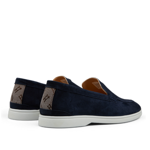 A pair of dark blue Herno suede slip-on loafers with white soles and branded canvas panels on the sides.