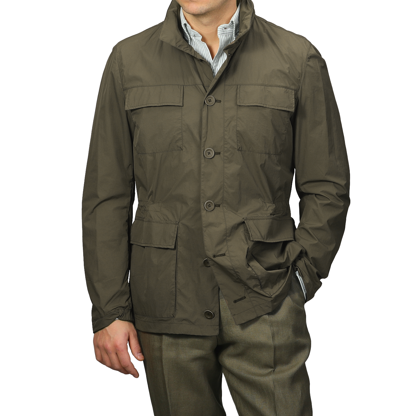 A person confidently wears a Herno Dark Green Ultralight Nylon Field Jacket, resistant to wind and rain, layered over a striped shirt with olive pants, one hand casually in a pocket.