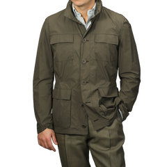 A person confidently wears a Herno Dark Green Ultralight Nylon Field Jacket, resistant to wind and rain, layered over a striped shirt with olive pants, one hand casually in a pocket.