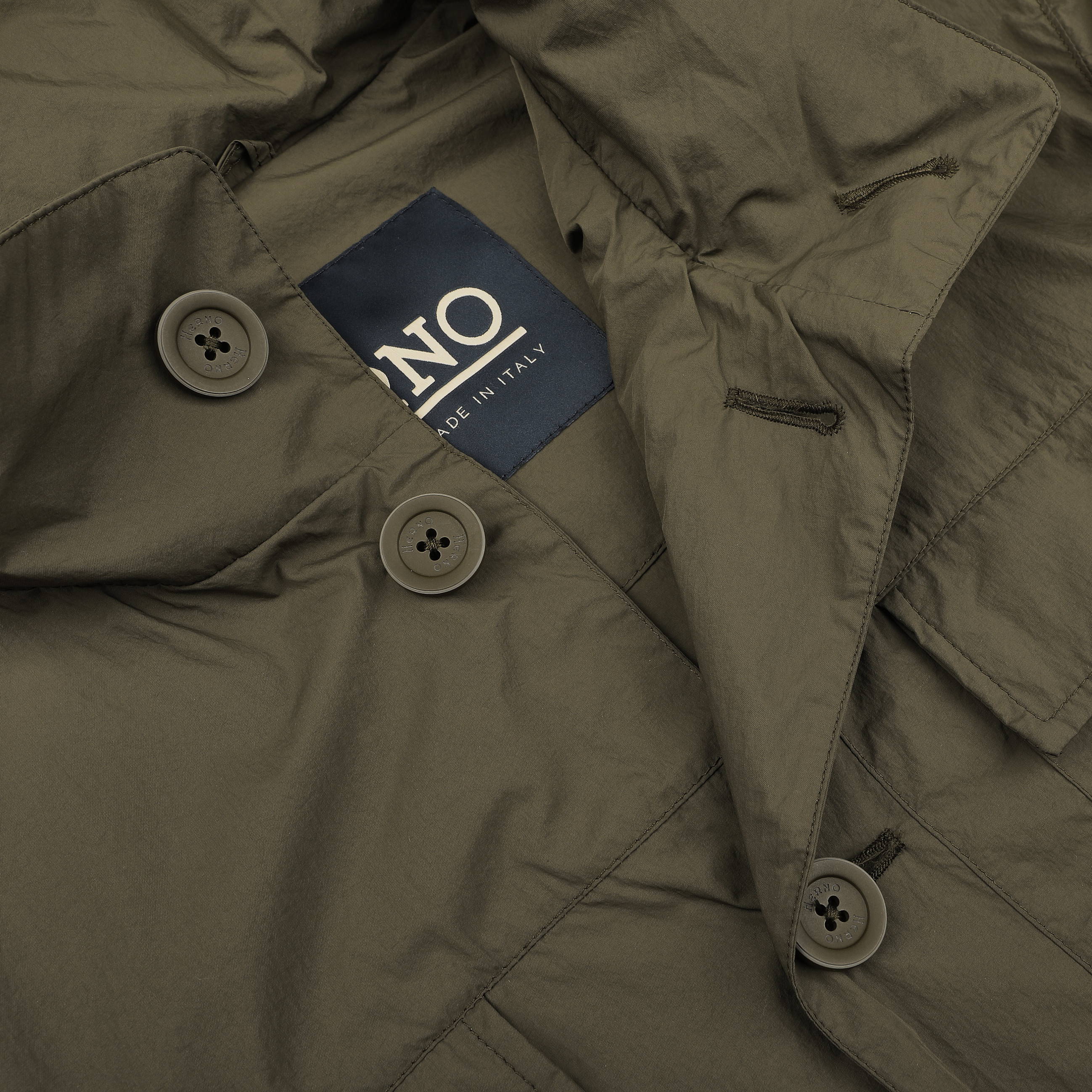 Close-up of a Herno field jacket in dark green, featuring a visible "MADE IN ITALY" label, crafted from ultralight nylon for wind and rain resistance.