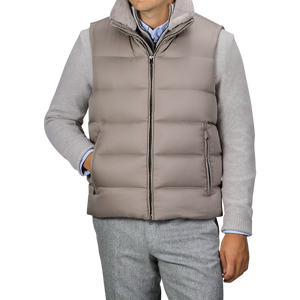 A person wearing the Herno Light Beige Nylon Goose Down Quilted Gilet over a light gray sweater and gray trousers. The water-repellent gilet is zipped up with hands in pockets.