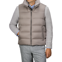 A person wearing the Herno Light Beige Nylon Goose Down Quilted Gilet over a light gray sweater and gray trousers. The water-repellent gilet is zipped up with hands in pockets.