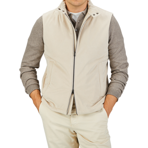 Man wearing a Herno Light Beige Suede Alcantara Zip Gilet over a gray long-sleeve shirt, paired with matching beige pants, standing with hands in his pockets against a plain background. This transitional style outfit perfectly blends comfort and elegance.