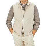 Man wearing a Herno Light Beige Suede Alcantara Zip Gilet over a gray long-sleeve shirt, paired with matching beige pants, standing with hands in his pockets against a plain background. This transitional style outfit perfectly blends comfort and elegance.